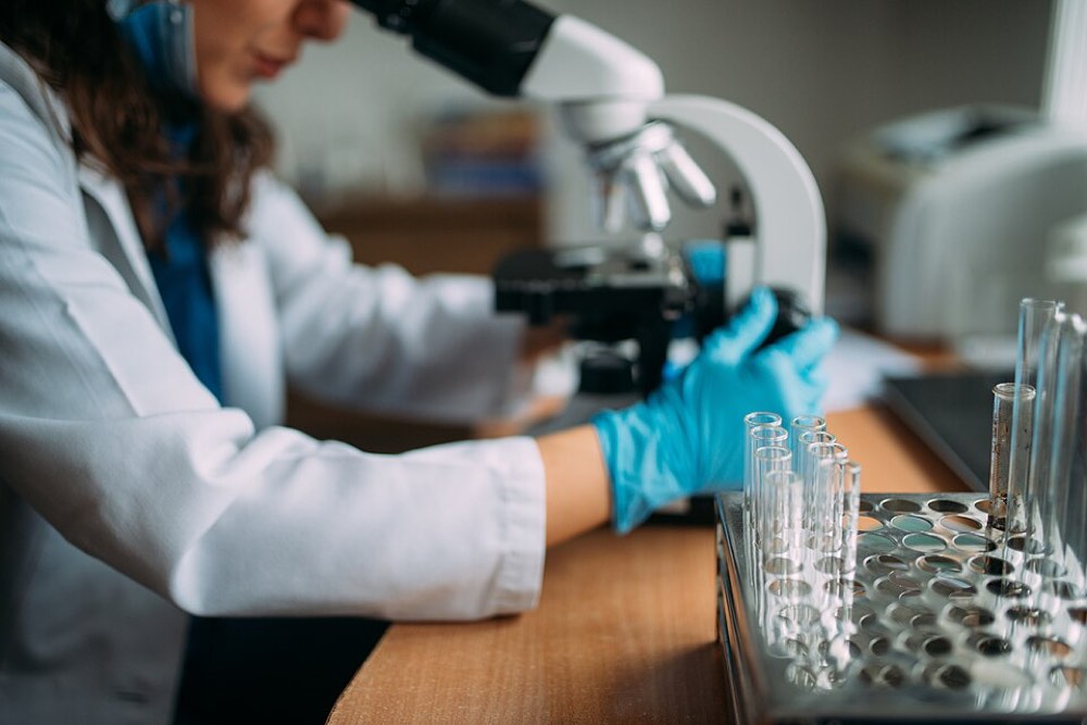 A laboratory researcher uses a microscope. Illustrative 2021 photograph; not an Orchestra Bio facility.